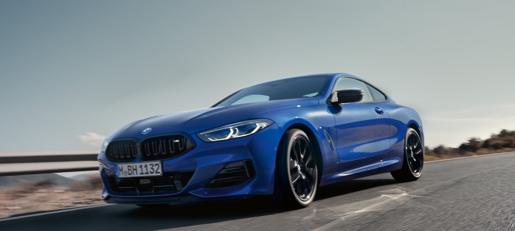 BMW 8 Series Coupé G15 LCI Facelift 2022 BMW M850i xDrive M Portimao blue metallic front view low-angle shot driving on country road in with hills in the background